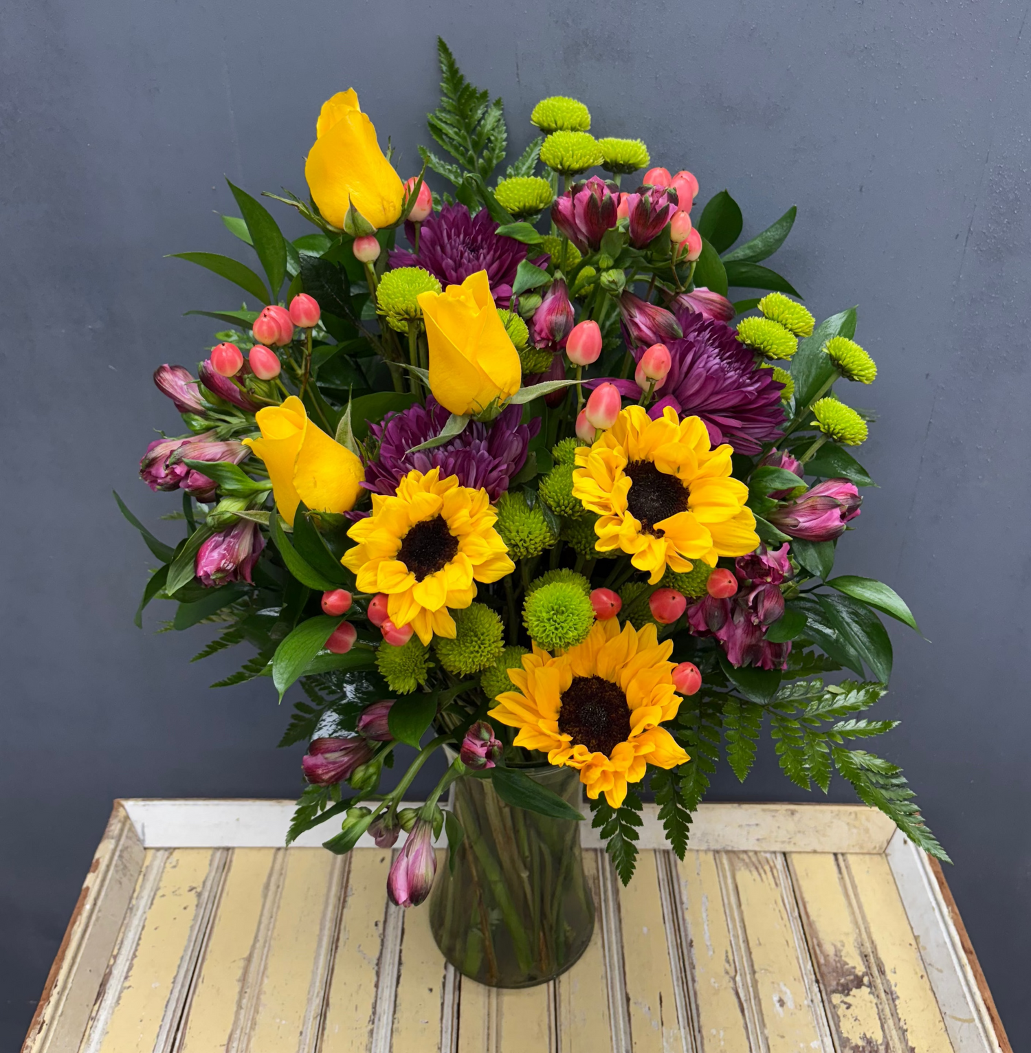 Bouquet of flowers with sunflowers and other colorful blooms in a vase on a wooden table.